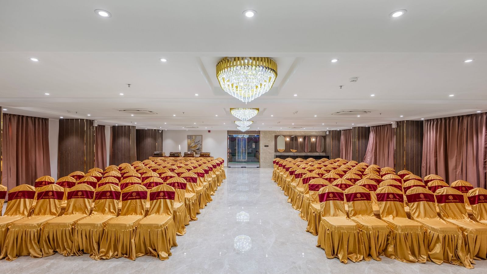 Lemonridge Hotels, KPHB | Banquet hall with rows of chairs and dining tables, set for an event.  Formal lighting fixtures.